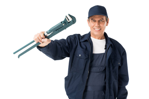 Cheerful plumber in uniform holding adjustable wrench isolated on white - Photo, Image