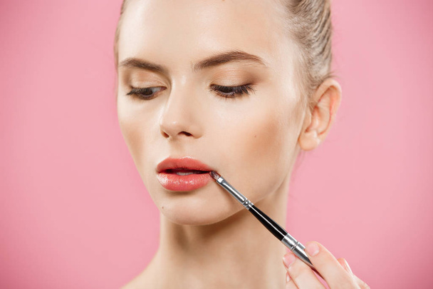 Beauty Concept - Woman applying red lipstick with pink studio background. Beautiful girl makes makeup. - Фото, зображення