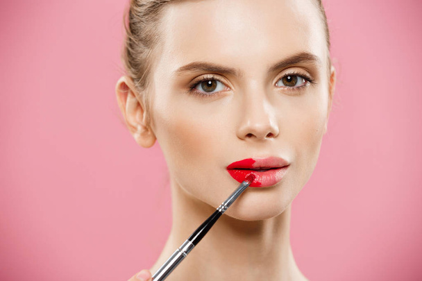 Beauty Concept - Mulher aplicando batom vermelho com fundo de estúdio rosa. Menina bonita faz maquiagem
. - Foto, Imagem