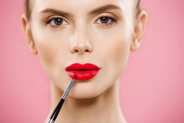 Beauty Concept - Woman applying red lipstick with pink studio background. Beautiful girl makes makeup. - 写真・画像