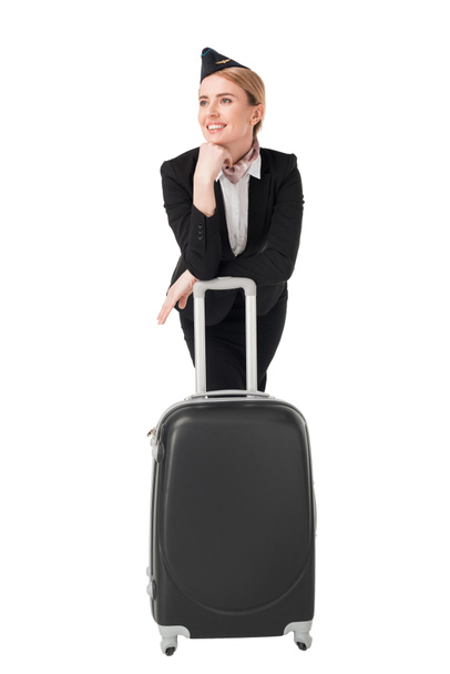 Jonge stewardess in uniform leunend op koffer geïsoleerd op wit - Foto, afbeelding