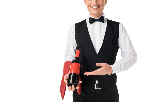 Camarero profesional sonriente presentando botella de vino aislada en blanco
 - Foto, Imagen