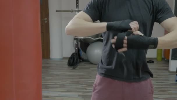 Young boxer wrapping boxing bandages around his hands before putting his gloves to train - Materiał filmowy, wideo