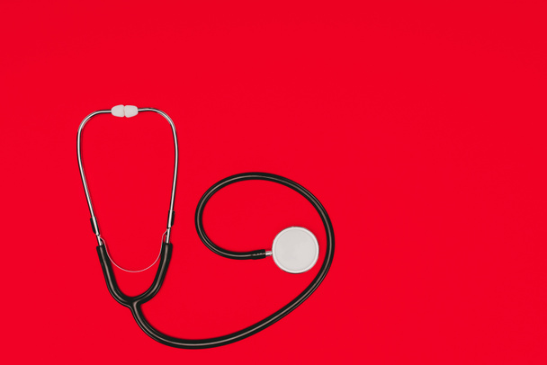 Draufsicht auf Stethoskop isoliert auf roter Oberfläche, Konzept Weltgesundheitstag - Foto, Bild