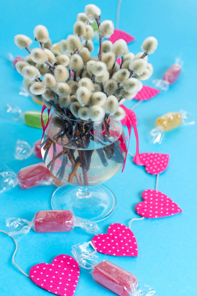 Feestelijke regeling in een glasvaas met twijgen bloeiwijzen. Heldere Candy slingers op een blauwe achtergrond. - Foto, afbeelding