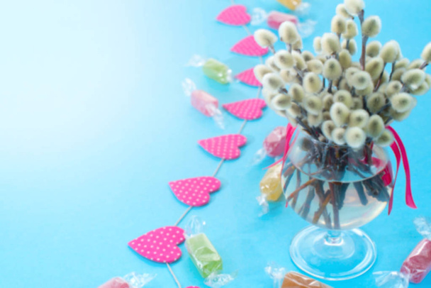 Sfocatura Disposizione festiva in un vaso di vetro con ramoscelli catkins. Luminose ghirlande di caramelle su sfondo blu
. - Foto, immagini