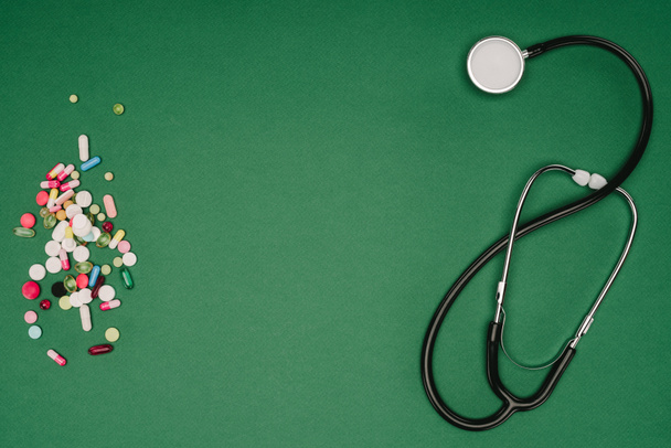 płaskie lay z pigułki ułożone i na białym tle na zielonym stole, świat zdrowia dzień koncepcji stetoskop - Zdjęcie, obraz