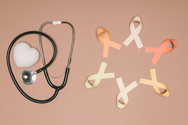 top view of arranged heart, stethoscope and colorful ribbons isolated on beige surface, world health day concept - Photo, Image
