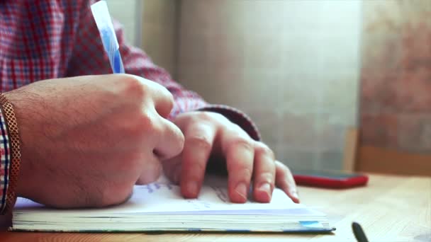 Hands writing on the paper.Young business man sitting at table drinking coffee, doing work writes in a book. Stock footage. - Video