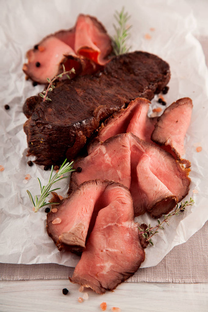 Нарізаний середній рідкісний смажений стейк з яловичини на білій дерев'яній кухонній тарілці
 - Фото, зображення