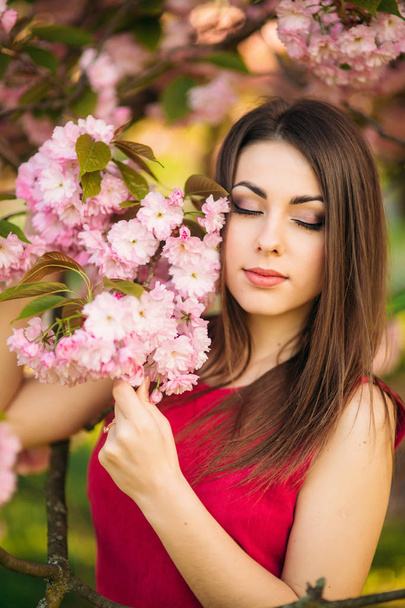 Portret młodej dziewczyny, pozowanie do zdjęć. Różowy kwitnienia drzew w tle. Wiosną. Sakura - Zdjęcie, obraz