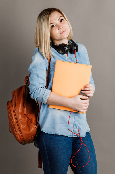 Όμορφη μαθήτρια που ποζάρει με βιβλία και χαμογελάει στην κάμερα. σε γκρίζο φόντο - Φωτογραφία, εικόνα