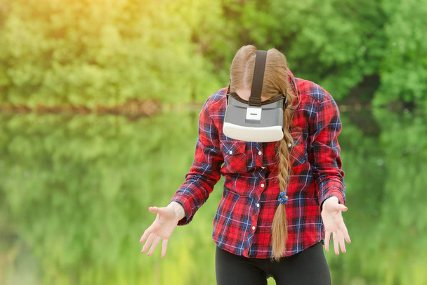 Girl in the helmet of virtual reality against the background of nature. Looking down - Foto, Imagem