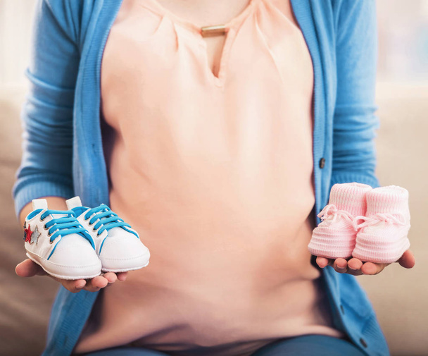 Pregnant woman is holding small shoes for the unborn baby - Photo, Image
