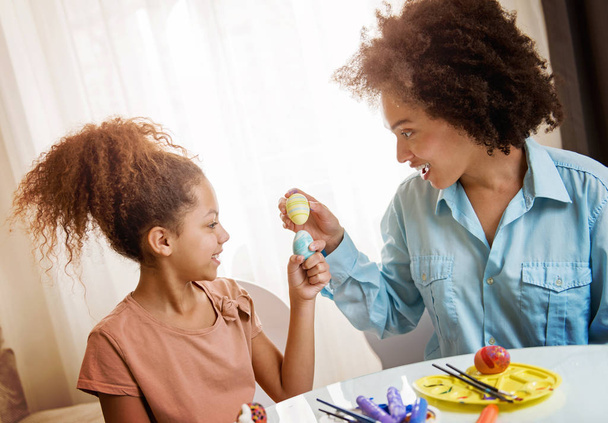 Beautiful African American woman and her daughter coloring Easter eggs at the table   - Valokuva, kuva