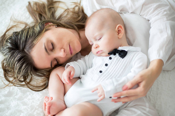 Mother and her baby son, sleeping on a big bed, soft back light - Foto, imagen