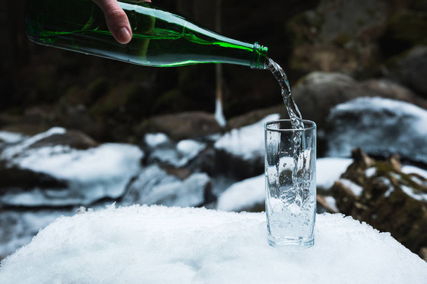 Ορυκτό μεταλλικό νερό που χύνεται από ένα πράσινο γυάλινο μπουκάλι σαφή ποτήρι ζέσεως. - Φωτογραφία, εικόνα