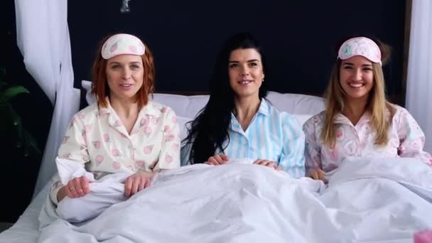 Üç kız pijama giymiş bir battaniye ile örtülü ve yatağına git. Yatakta pampering eğlenceli. - Video, Çekim