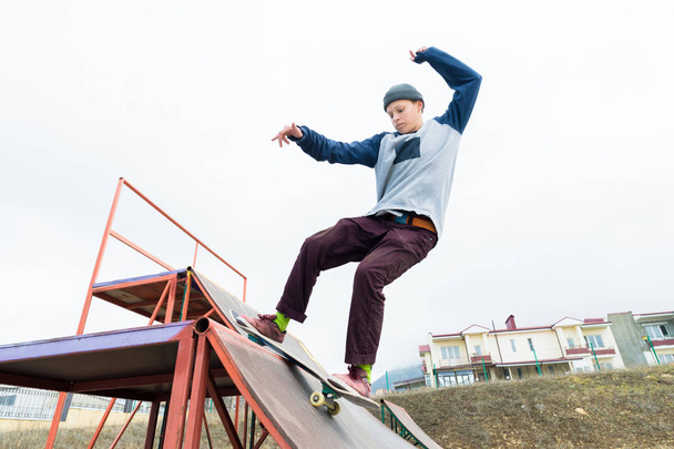 Teen skater in a hoodie sweatshirt and jeans slides over a railing on a skateboard in a skate park - Foto, Imagen