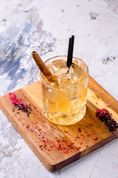 Close up, brown alcoholic cocktail with whiskey, ice cubes decorations on a wooden board, gray background. Bar alcohol menu, strong drink for evening. Space for text design, selective focus. - Фото, изображение