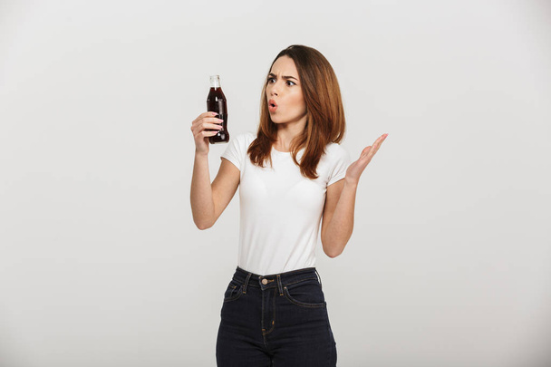 Shocked young woman holding bottle with soda. Looking aside. - Foto, immagini