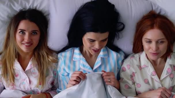 Vista dall'alto, tre belle ragazze vanno a letto in pigiama carino in un letto accogliente ricordando l'infanzia. Sorelle amorevoli
. - Filmati, video