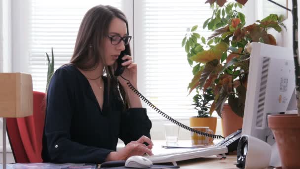 Vrouwelijke receptioniste werken op de computer en praten over telefoon in callcenter - Video