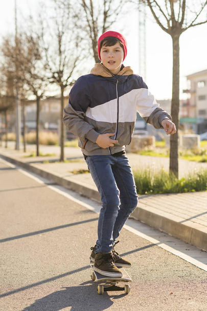 Skater-teenager wearing a hat boarding on the street - Фото, изображение