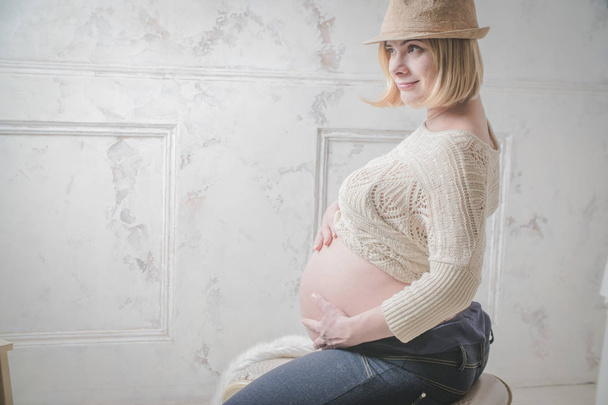 happy young pregnant woman wearing hat and posing on grey background - Photo, Image