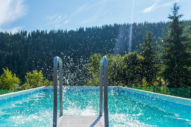 frische Spritzer Poolwasser im Freien an einem sonnigen Sommertag mit grünem Wald im Hintergrund - Foto, Bild