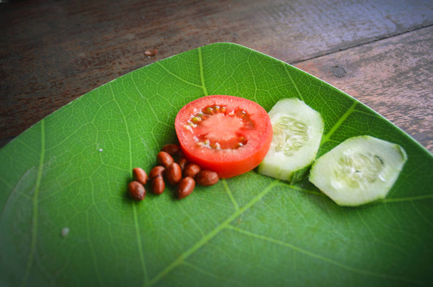 Snack végétalien d'arachides, tranche de tomate et tranches de concombre dans un plat de feuilles conçu
. - Photo, image