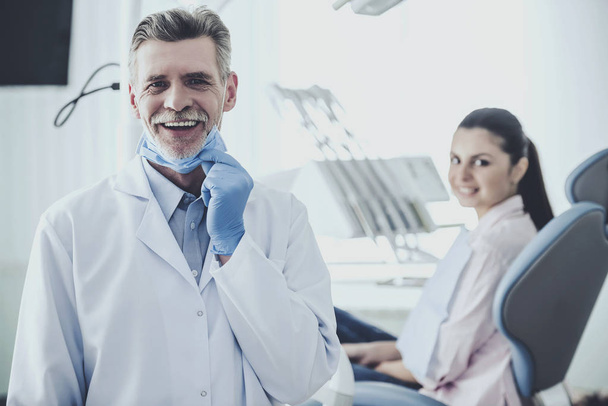 Portrait of a smiling senior dentist on the background his patient in dental clinic - Fotó, kép