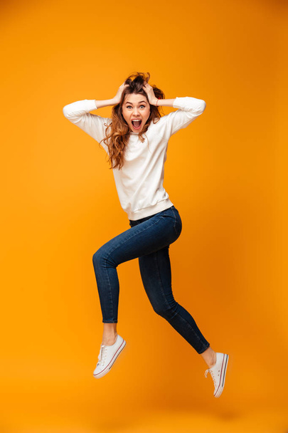 Full length image of Shocked brunette woman in sweater jumping - Фото, изображение
