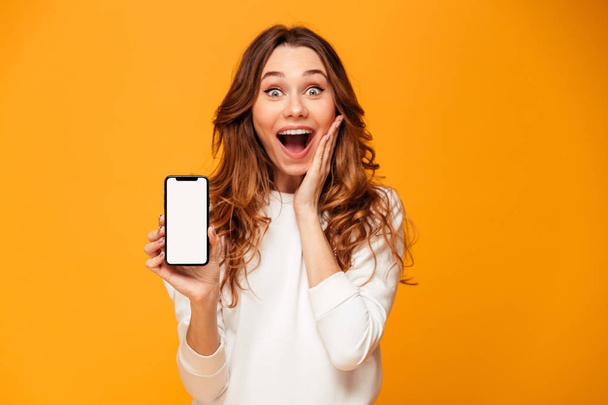 Shocked brunette woman in sweater showing blank smartphone scree - Photo, image