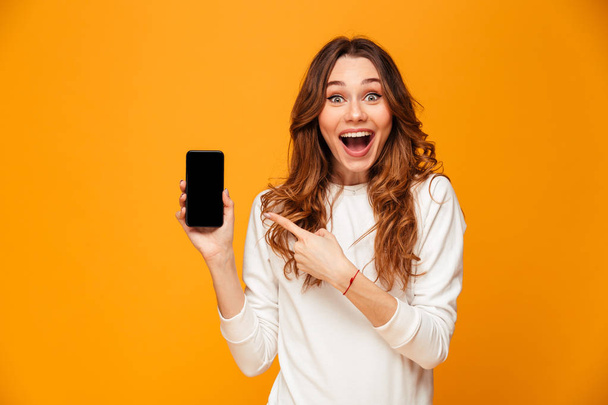 Surprised happy brunette woman in sweater showing blank smartphone screen - Фото, изображение