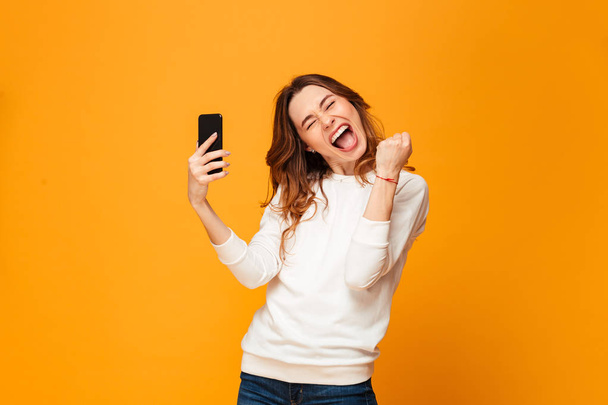 Happy screaming brunette woman in sweater holding smartphone - Photo, image