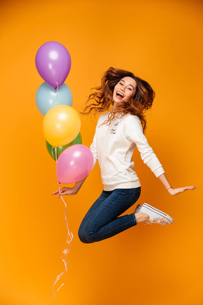 Excited young woman jumping isolated holding balloons. - Foto, afbeelding