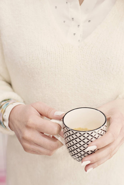 Woman with white sweater and beautiful manicure holding cup of hot coffee - Photo, Image