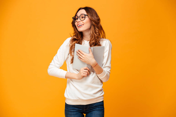 Pleased brunette woman in sweater and eyeglasses hugging book - Фото, зображення