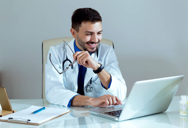 Confident male doctor working with his laptop in the office. - 写真・画像
