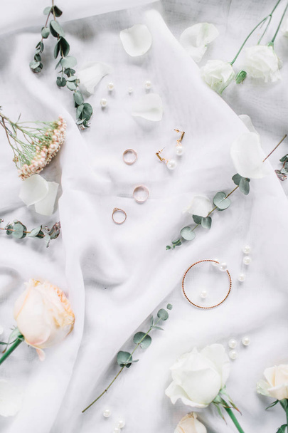Svatební složení s větví eukalyptu, svatební prsteny, růžový květ na bílé textilní pozadí. Plochá ležel, horní pohled slavnostní svatební módní koncept. - Fotografie, Obrázek
