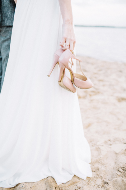 Zapatos de tacón alto en las manos de mujer joven en la playa
. - Foto, imagen