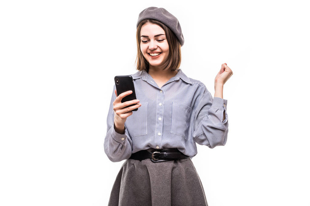 Fiatal boldog nő visel a svájcisapka, telefonnal a kezében olvasni jó hír, izgatott érzelmek elszigetelt fehér background - Fotó, kép