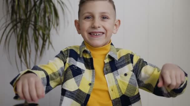 Charming boy blonde with blue eyes smiles and raises arms up looking happy, isolated on white. Happy boy, victory, happy moment in life. In white background, indoors - Materiał filmowy, wideo
