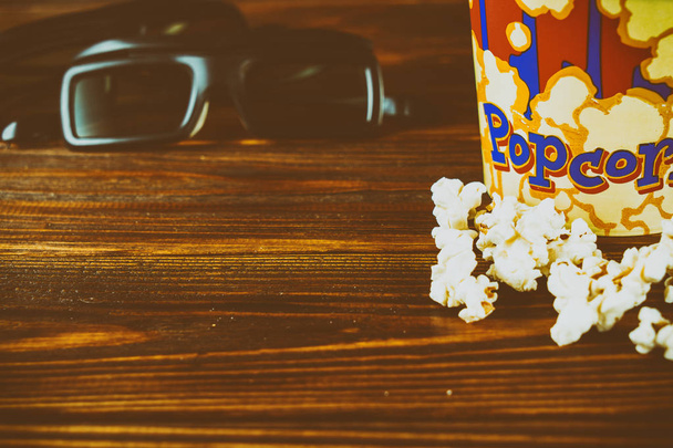 Popcorn and glasses for watching 3d movies on a wooden background. Toned photo - Photo, Image