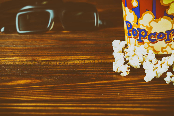 Popcorn and glasses for watching 3d movies on a wooden background. Toned photo - Photo, Image