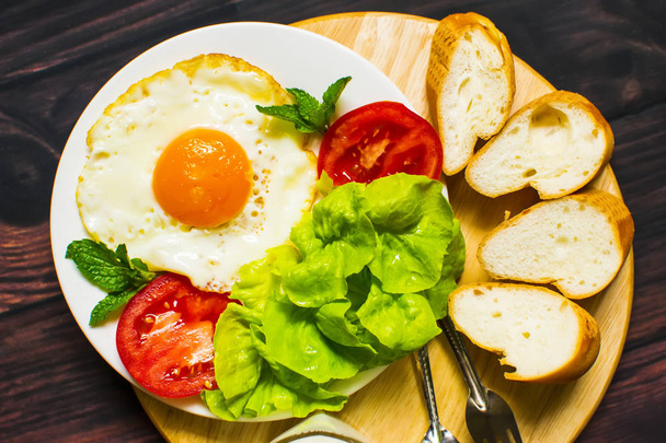 Breakfast with bread, fried eggs, milk and vegetables and fried tomato pieces on wood background - Photo, image