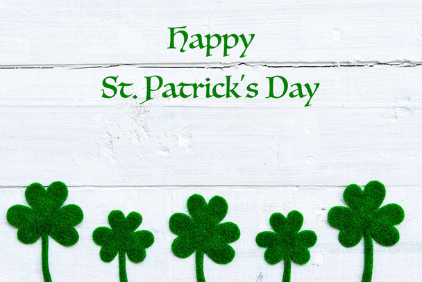 Happy St Patricks Day message and a lot of green paper clover leaf on white wooden background - Фото, зображення