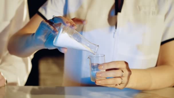 Experiments in a chemistry lab. Young woman scientist mixing reagents from glass flasks - Imágenes, Vídeo