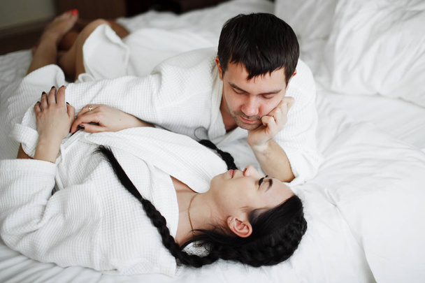 Νεαρή σύζυγος και η σύζυγος του λευκού τριχώματος παίζουν και το χαμόγελο στο κρεβάτι σε ένα - Φωτογραφία, εικόνα